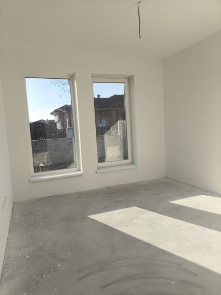 A room in a family house with a bare floor and large windows, light streaming in.