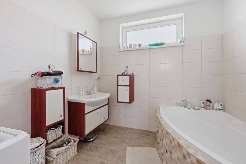 Bathroom in a family house with a bathtub, sink, cabinets, and a window.