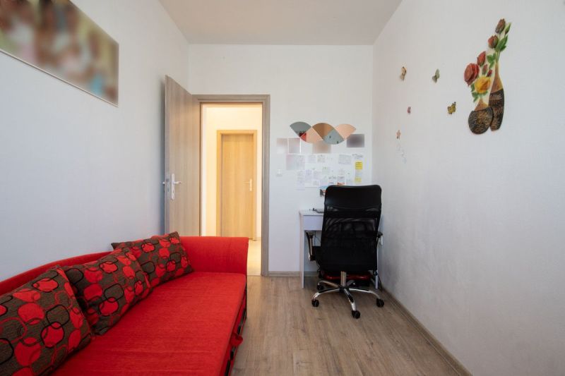 A room in a family house with a red sofa, a desk, and a wooden-patterned floor.