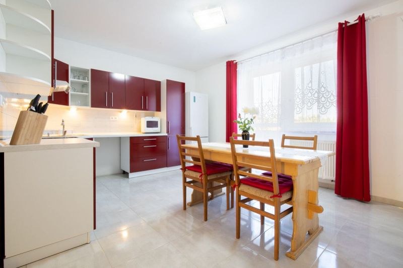 A kitchen in a family house with red cabinets, a dining table, and curtains.