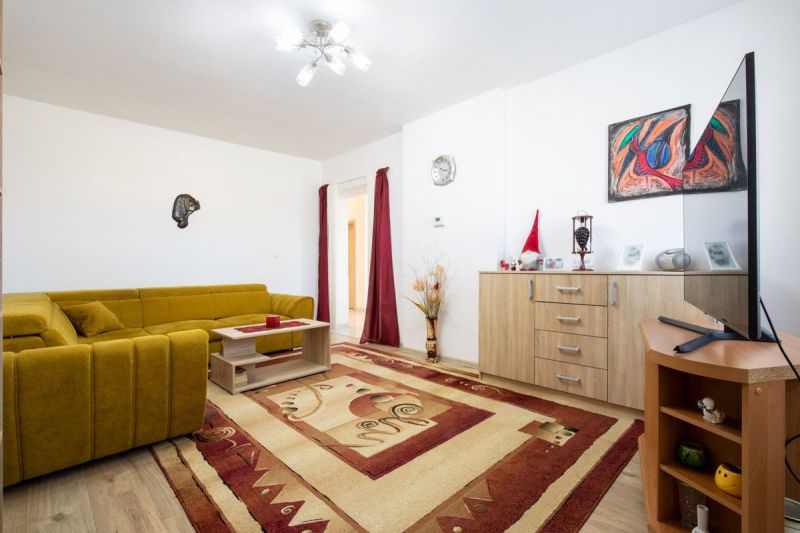 A living room in a family house with a mustard-colored sofa, a decorative carpet, and wooden decor.