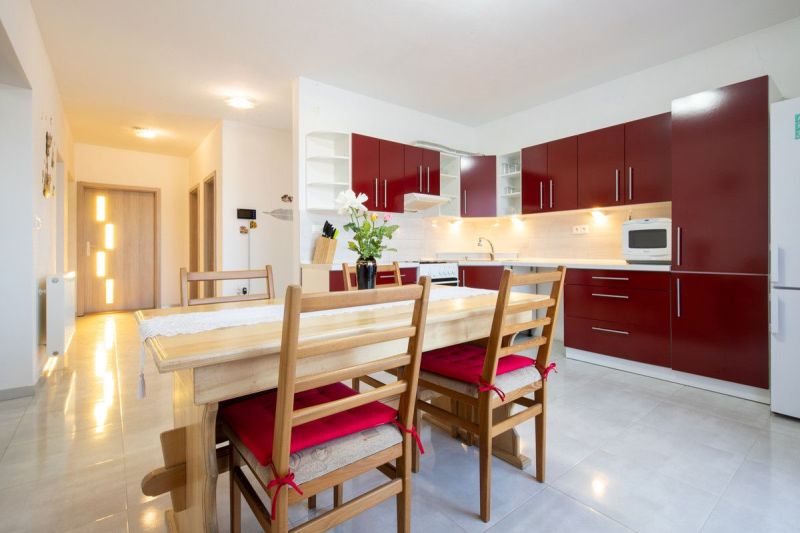 A kitchen in a family house with red cabinets, a dining table, and a light floor.
