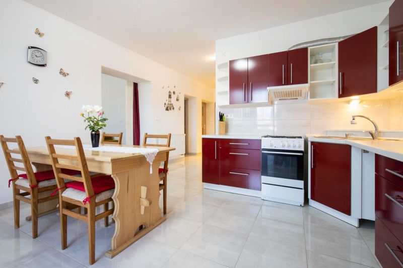 A kitchen in a family house with red cabinets and a wooden dining table.
