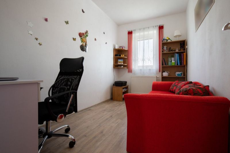 An office in a family house with a red sofa and wood-patterned flooring.