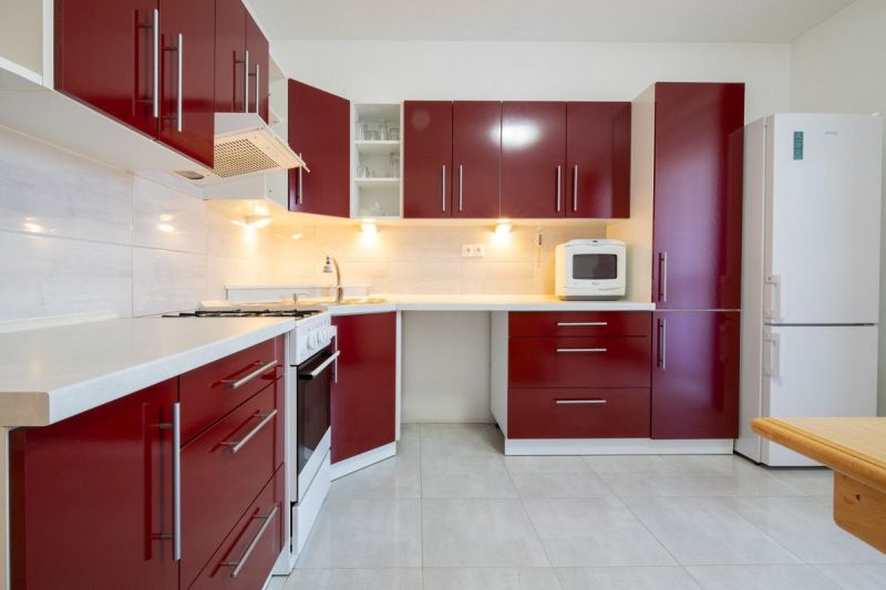 A kitchen with red cabinets in a family house, white appliances, light tiles.