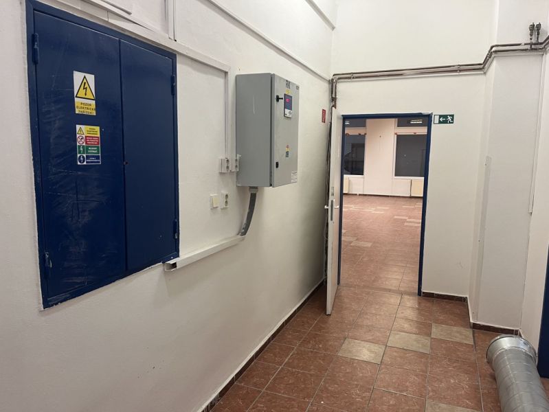 A corridor with an electrical equipment cabinet leading to commercial premises with tiling.