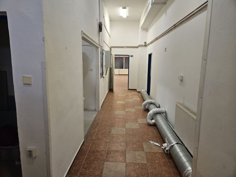 A corridor with light walls, tiles, and piping in commercial premises.