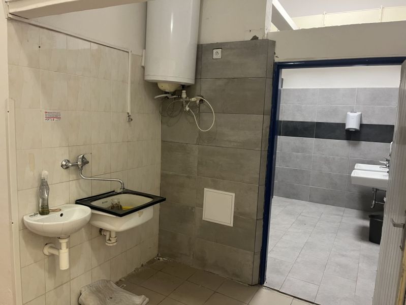 Interior of commercial premises with a sink and a boiler, adjacent to a tiled bathroom.