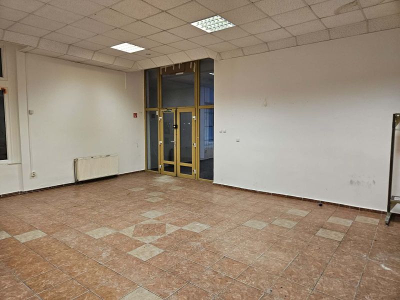An empty commercial space with tiled flooring, white walls, and large windows.