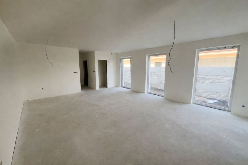 A spacious room with three windows and an unfinished floor in a family house.