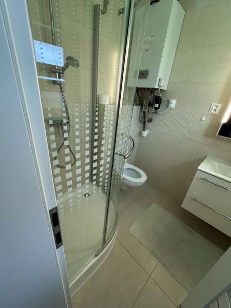 A bathroom in a studio apartment with a corner shower, sink, and toilet.