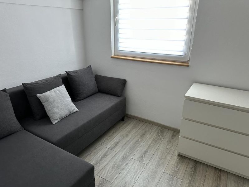 Gray sofa and white dresser in a studio apartment with wood-patterned flooring.