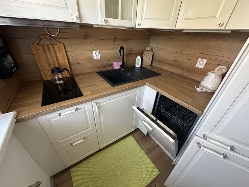 A kitchen in a studio apartment with a wooden decor countertop, built-in dishwasher, and sink.