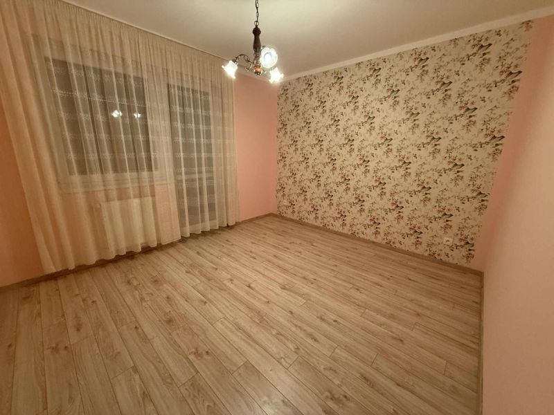 A room with patterned wallpaper, curtains, and a floor with a wooden decor in a three-room apartment.
