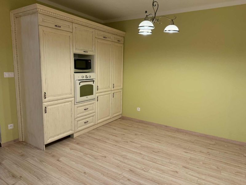 Kitchen cabinet with microwave and oven, green walls, floor with wooden decor.