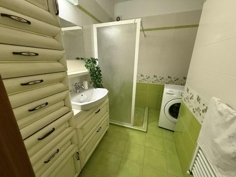 A bathroom in a 3-room apartment with a shower, washing machine, and decorative tiles.