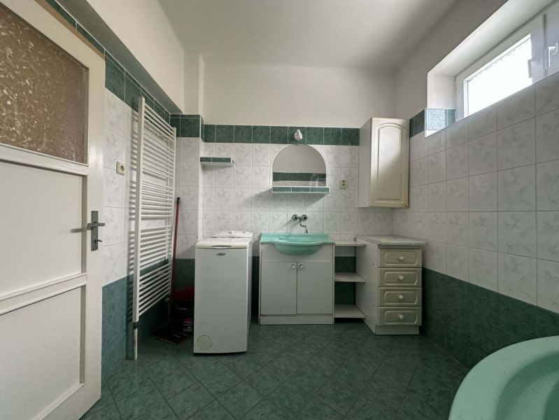 Bathroom in a family house with a washing machine, green sink, and tiles.