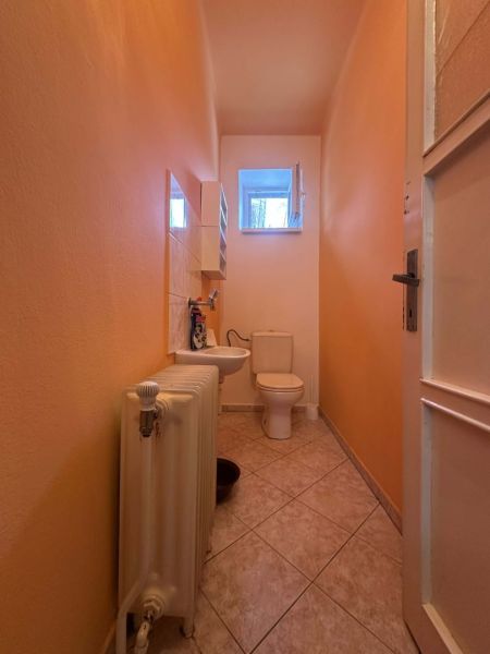 A toilet in a family house with a radiator, a sink, and a small window.
