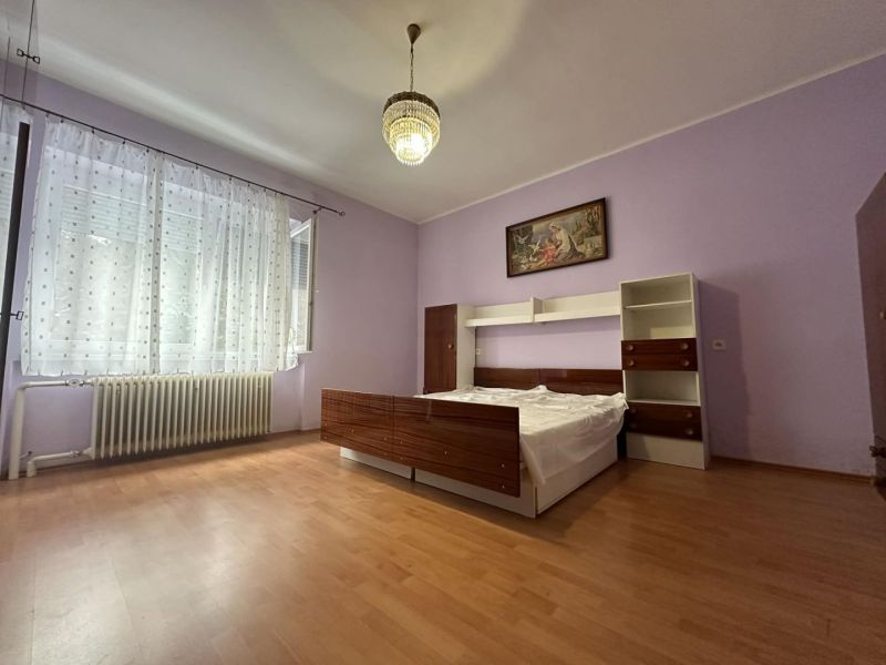 A room in a family house with a bed, purple walls, and a wood-patterned floor.