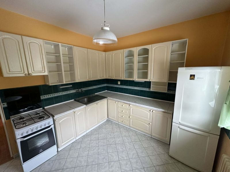 A kitchen in a family house with cream cabinets, dark green tiles, and a white appliance.