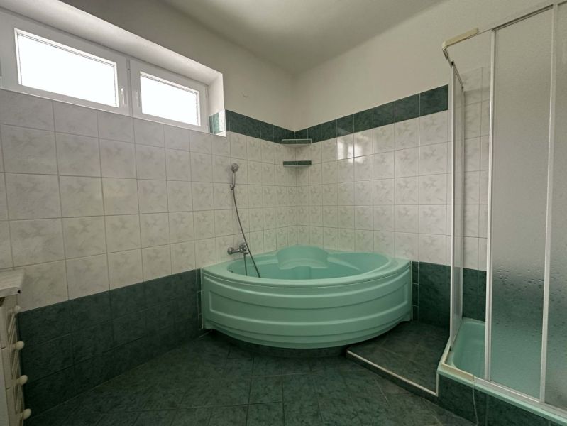 A bathroom in a family house with a corner bathtub and a shower, green tiles.