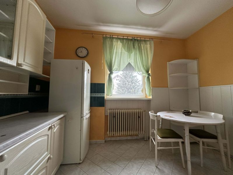 A kitchen in a family house with white furniture, a refrigerator, and a table for two people.