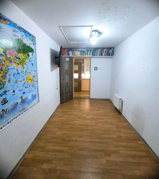 A room in a family house with a wooden decor floor, a map on the wall, and a bookshelf with books.
