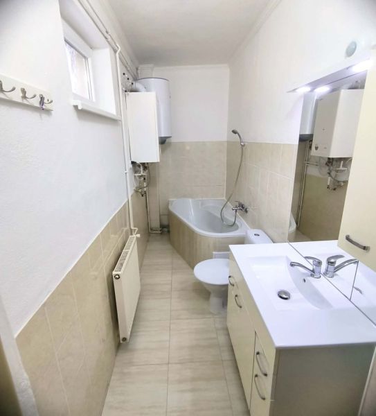 A bathroom in a family house with a bathtub, sink, and radiator, with light wall tiles.