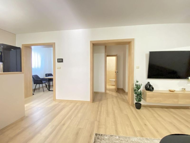 Interior of a 3-room apartment with a wood-patterned floor and a TV on the wall.