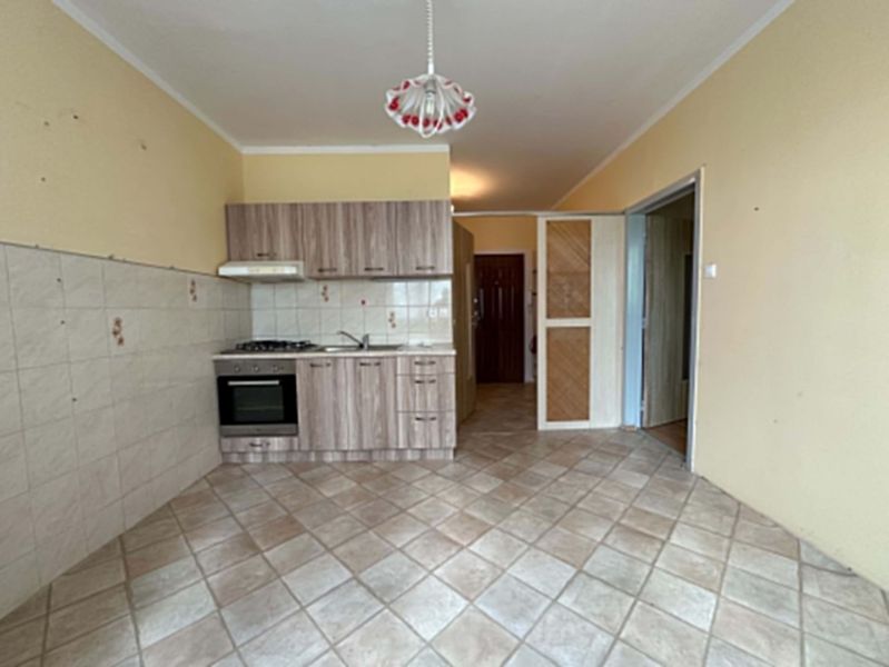 A kitchen in a studio apartment with a tiled floor and light-colored furniture.