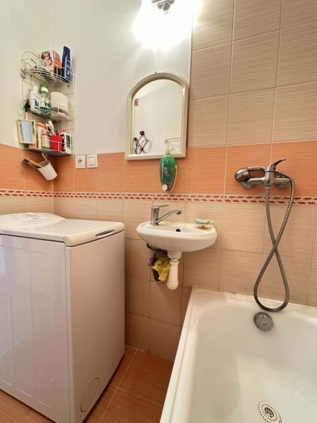 A bathroom in a studio apartment with a bathtub, washing machine, and small sink.