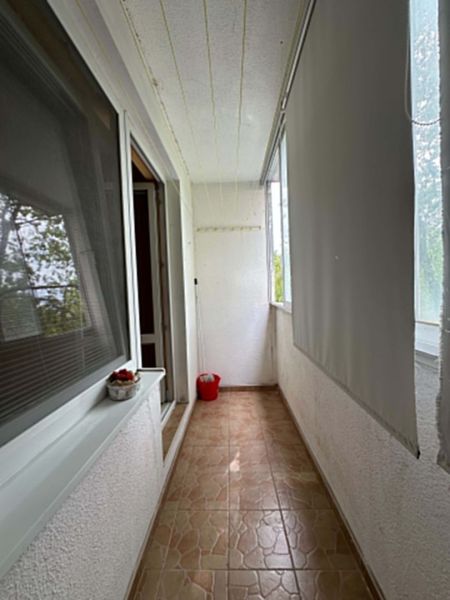 A narrow loggia with flowers and blinds in a one-room apartment, a floor with a stone decor.