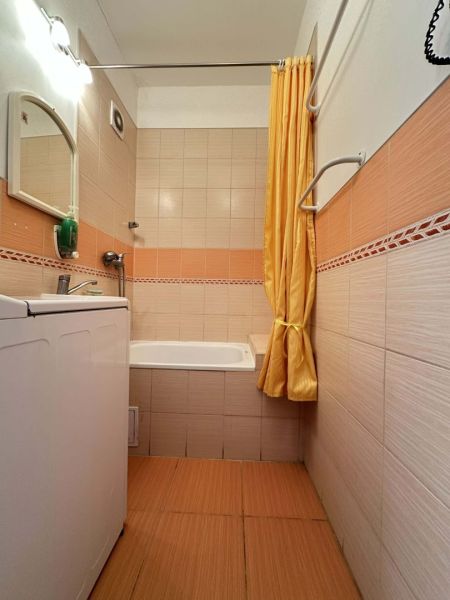Bathroom with a bathtub and a washing machine in a studio apartment with orange tiles.