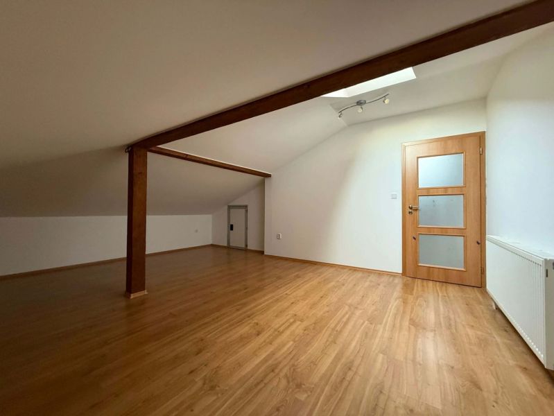 Attic room in a 3-room apartment with a wooden decor floor and wooden beams.