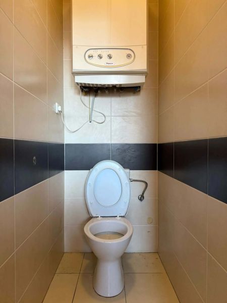 A toilet with tiles and a water heater in a 3-room apartment.