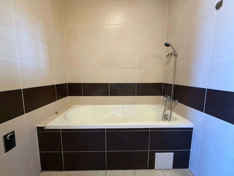 A bathroom with a built-in bathtub and patterned tiling in a three-room apartment.
