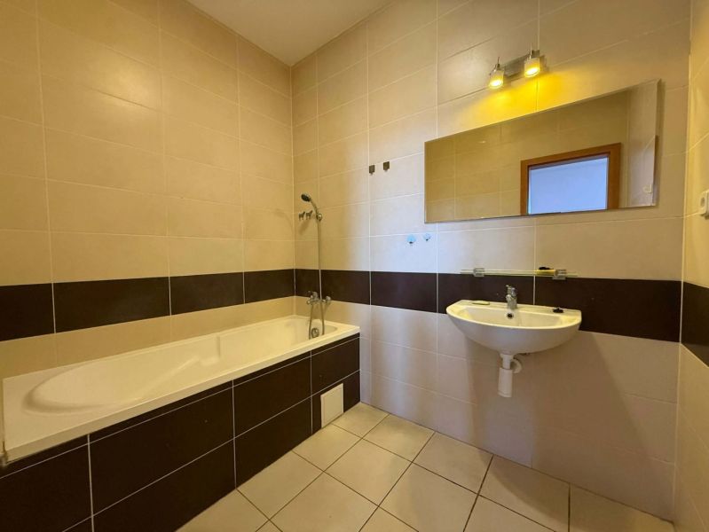 The bathroom with a bathtub in the 3-room apartment has light tiles and a mirror above the sink.