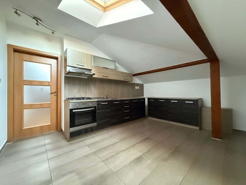 A kitchen in the attic of a 3-room apartment with dark cabinets and a skylight.