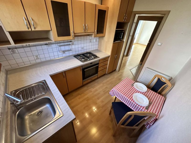 A kitchen in a 3-room apartment with a stove, sink, table, and a floor with a wooden decor.