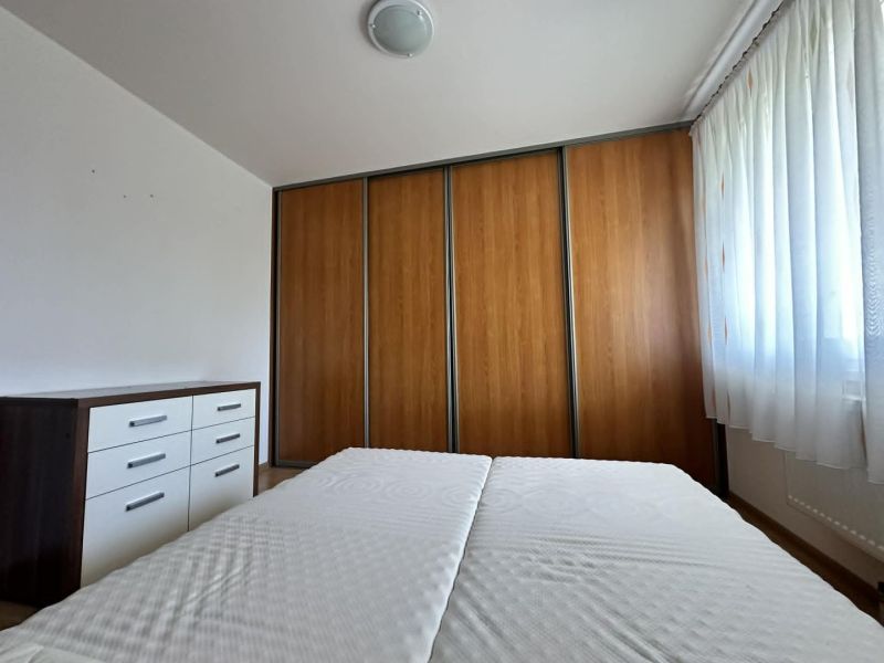 A bedroom with a wardrobe featuring a wooden decor and a dresser in a three-room apartment.