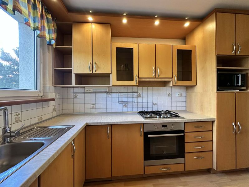 A kitchen in a 3-room apartment with wooden cabinets and white tiles.