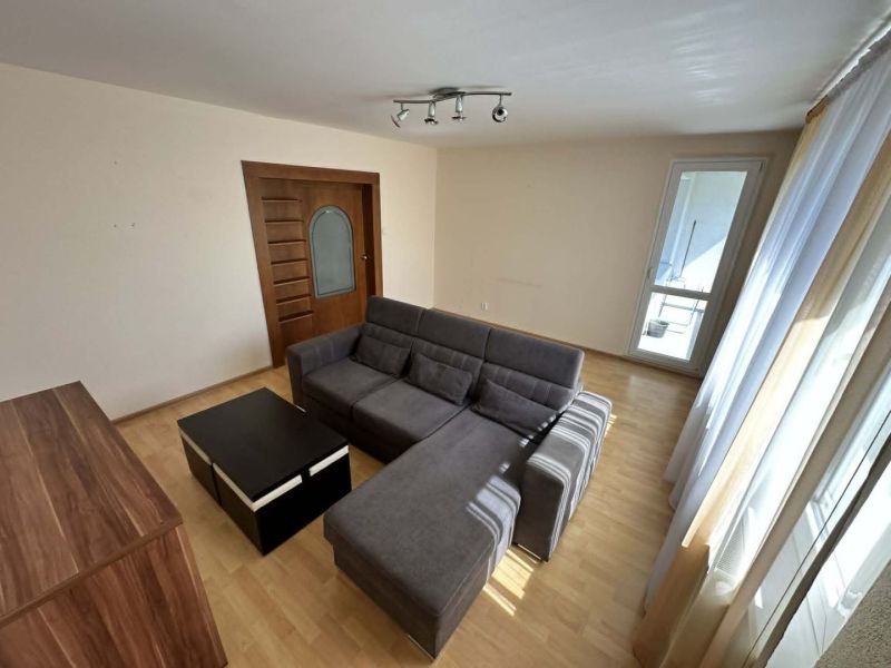 A bright living room with a corner sofa and a wooden decor floor in a 3-room apartment.