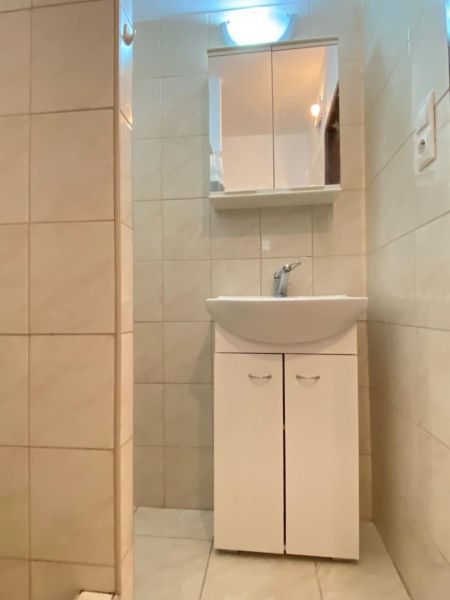 Bathroom in a studio apartment with a sink, mirror, and light tiles.