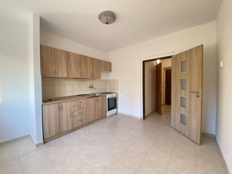 A kitchen in a studio apartment with tiled flooring and wooden decor cabinets.