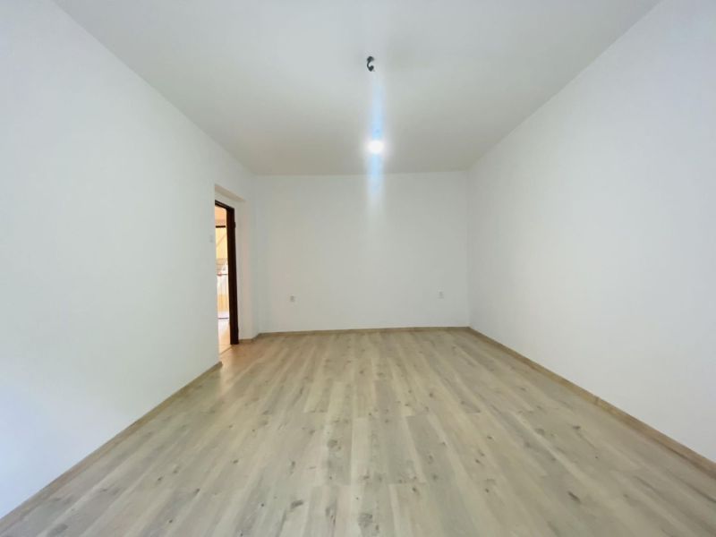 A spacious room with white walls and a floor with a wooden decor in a studio apartment.