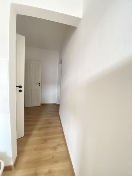 A hallway in a one-room apartment with a wooden decor floor and white walls.