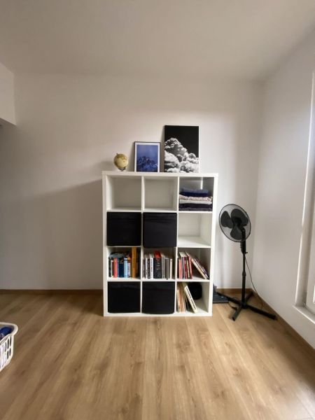 Bookshelf with books and decorations, fan, wooden decor floor, studio apartment.
