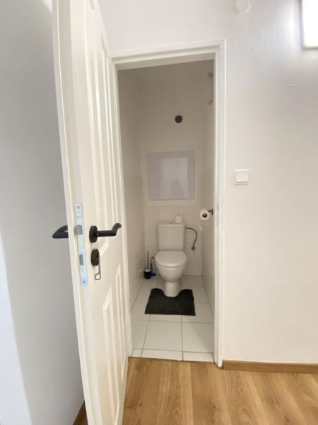 A toilet in a one-room apartment with a wooden decor floor and white tiles.