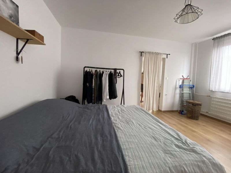 A bedroom in a studio apartment with a bed, a clothes rack, and a wooden decor floor.