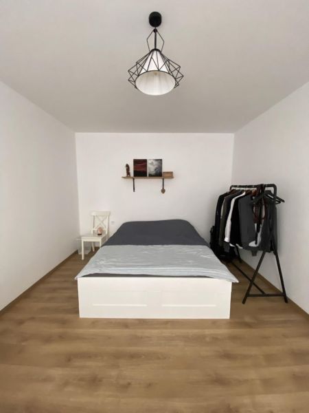A bedroom in a one-room apartment with a bed, a shelf, and a floor with a wooden decor.